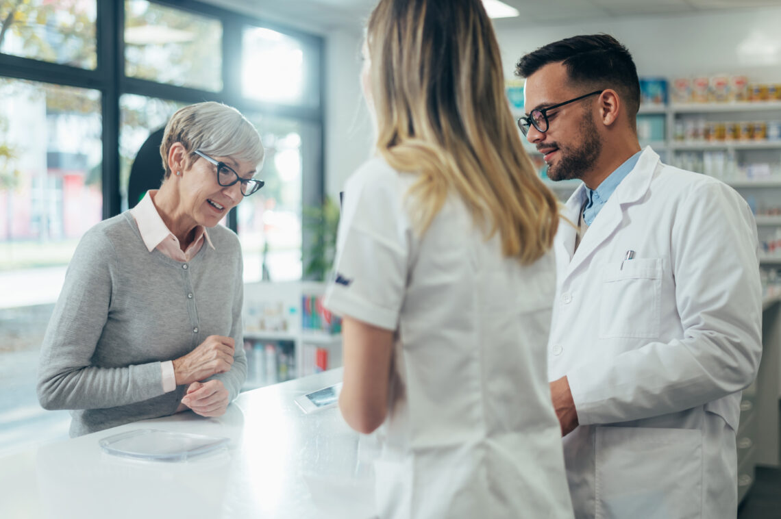 Two Pharmacist Giving Prescription Medications To Senior Female Customer In A Pharmacy